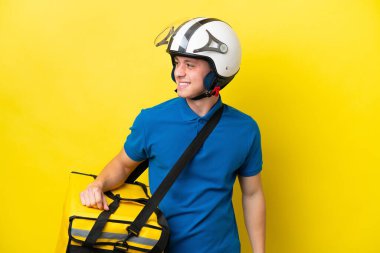 Sırt çantalı genç Brezilyalı adam sarı arka planda izole edilmiş, yana bakıyor ve gülümsüyor.