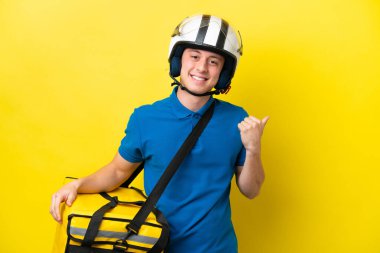Young Brazilian man with thermal backpack isolated on yellow background pointing to the side to present a product