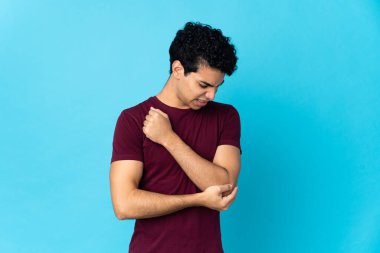 Genç Venezuelalı adam mavi arka planda izole edilmiş, dirsek ağrısı var.