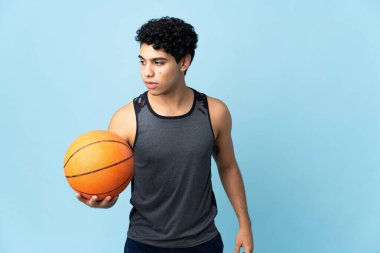 Genç Venezuelalı adam mavi arka planda izole edilmiş basketbol oynuyor.