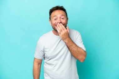 Mavi arka planda izole edilmiş orta yaşlı beyaz bir adam mutlu ve gülümsüyor.