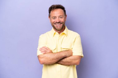 Mor arka planda izole edilmiş orta yaşlı beyaz bir adam kollarını ön cephede çapraz tutuyor.