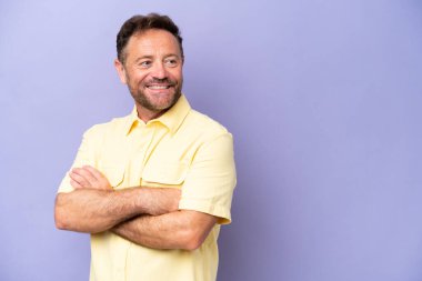 Orta yaşlı beyaz bir adam mor arka planda izole edilmiş, kolları bağlı ve mutlu.