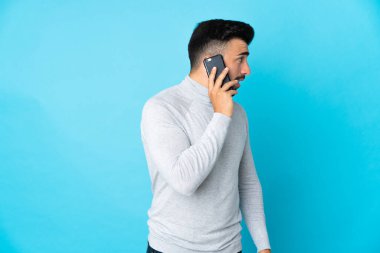 İzole edilmiş mavi arka planı olan beyaz bir adam cep telefonuyla sohbet ediyor.