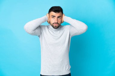 İzole edilmiş mavi arka planı olan beyaz bir adam hayal kırıklığına uğramış ve kulaklarını kapatmış.