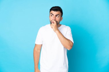 İzole edilmiş mavi arka planı olan beyaz bir adamın şüpheleri ve şaşkın bir yüz ifadesi var.