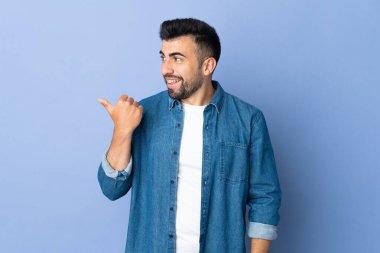 İzole edilmiş mavi arka planda beyaz bir adam bir ürünü sunmak için kenarı işaret ediyor.