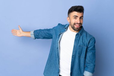 İzole edilmiş mavi arka planda beyaz bir adam. Davet etmek için ellerini yana uzatıyor.