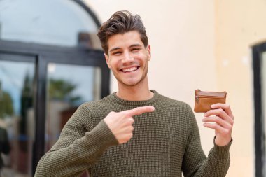 Genç beyaz bir adam açık havada bir cüzdan tutuyor ve ona doğrultuyor.