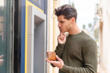 Açık havada ATM kullanan genç beyaz bir adam.