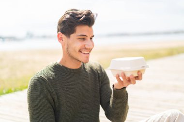 Dışarıdaki genç beyaz adam bir kutu paket yemek alıyor.