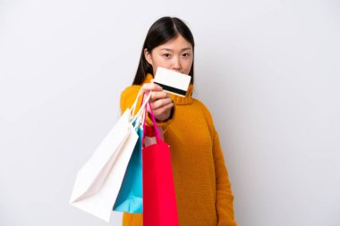 Beyaz arka planda izole edilmiş genç bir Çinli kadın elinde alışveriş çantaları ve bir kredi kartı tutuyor.