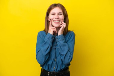 Sarı arka planda izole edilmiş genç bir İngiliz kadın mutlu ve hoş bir ifadeyle gülümsüyor.