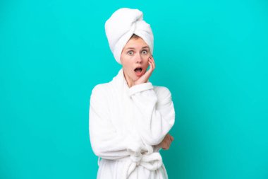 Bornozlu genç bir kadın mavi arka planda izole edilmiş, sağa bakarken şaşırmış ve şok olmuştu.