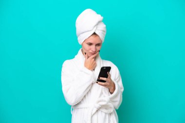 Bornozlu genç bir kadın mavi arka planda izole edilmiş düşünüyor ve bir mesaj gönderiyor.