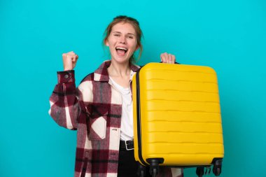 Genç İngiliz kadın mavi arka planda izole edilmiş seyahat valiziyle tatilde.