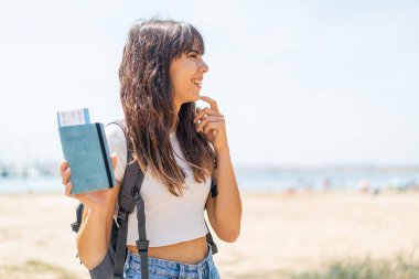 Pasaportu elinde tutan genç bir kadın bir fikir üretiyor ve diğer tarafa bakıyor.