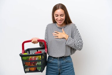 Young Rumanian woman holding a shopping basket full of food isolated on white background smiling a lot