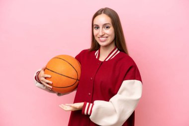 Beyaz tenli genç basketbolcu kadın, pembe arka planda izole edilmiş, davet edildiği için ellerini yana açıyor.