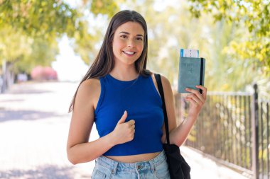 Dışarıda elinde pasaport tutan genç, güzel bir Brezilyalı kadın. Başparmakları havada, çünkü iyi bir şey oldu.