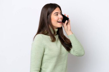 Beyaz arka planda izole edilmiş genç Brezilyalı kadın cep telefonuyla sohbet ediyor.