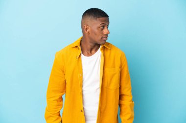 Mavi arka planda izole edilmiş genç latin adam yan tarafa bakıyor.