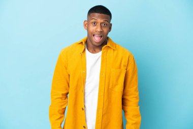 Mavi arka planda yalıtılmış genç latin adam, şaşırmış yüz ifadesi ile