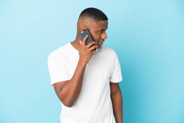 Genç latin adam mavi arka planda izole edildi. Cep telefonuyla biriyle sohbet ediyor.
