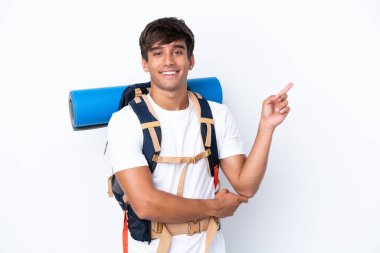 İzole edilmiş beyaz arka plan üzerinde büyük bir sırt çantası olan genç dağcı kadın parmağını yana doğru gösteriyor.