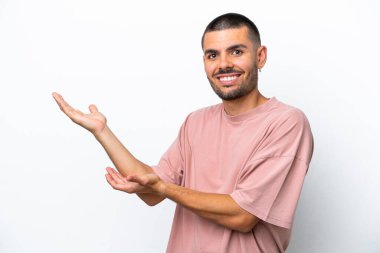 Beyaz arka planda soyutlanmış beyaz tenli genç adam davet edilmek için ellerini yana uzatıyor.