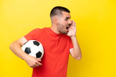 Sarı arka planda izole bir şekilde futbol oynayan beyaz bir adam ağzı açık bağırıyor.