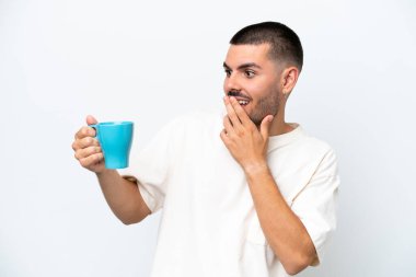 Kafkasyalı genç bir adam elinde kahve fincanı tutarken beyaz arka planda şaşırmış ve şok olmuş bir yüz ifadesi vardı.