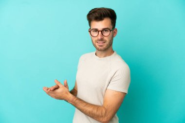 Beyaz tenli yakışıklı adam mavi arka planda izole edilmiş alkışlıyor.