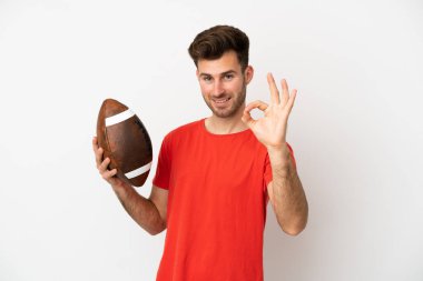 Beyaz arka planda ragbi oynayan beyaz tenli genç adam parmaklarıyla işaret veriyor.