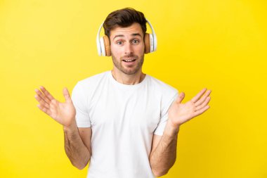 Sarı arka planda izole edilmiş beyaz yakışıklı genç adam şaşırdı ve müzik dinliyor.