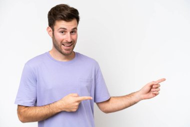 Beyaz arka planda izole edilmiş genç beyaz adam şaşırmış ve işaret ediyor.