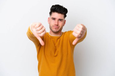 Beyaz arka planda izole edilmiş genç beyaz bir adam baş parmağını iki eliyle aşağı gösteriyor.