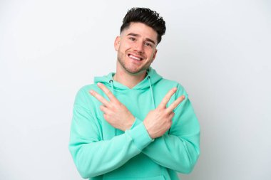 Beyaz arka planda izole edilmiş genç beyaz adam gülümsüyor ve zafer işareti gösteriyor.