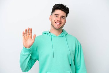 Beyaz arka planda izole edilmiş genç beyaz bir adam mutlu bir ifadeyle selamlıyor.