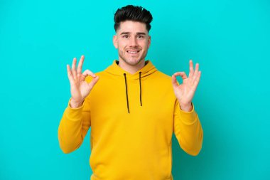 Mavi arka planda izole edilmiş beyaz bir adam iki eliyle tamam işareti gösteriyor.