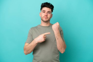 Kafkasyalı genç adam mavi arka planda izole edilmiş. Geç kalma jesti yapıyor.