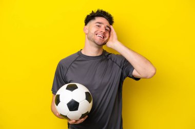 Yakışıklı genç futbolcu. Sarı arka planda izole edilmiş. Çok gülümsüyor.