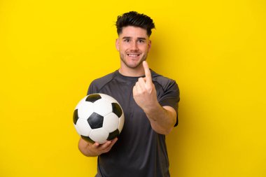 Yakışıklı genç futbolcu sarı arka planda izole edilmiş bir şekilde geliyor.