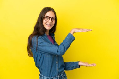 Sarı arka planda izole edilmiş genç bir Fransız kadın ilan vermek için kopyalama alanı tutuyor.