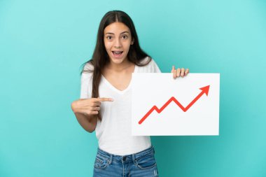 Genç Fransız kadın mavi arka planda izole edilmiş. Elinde büyüyen bir istatistik oku sembolü olan bir tabela var ve işaret ediyor.