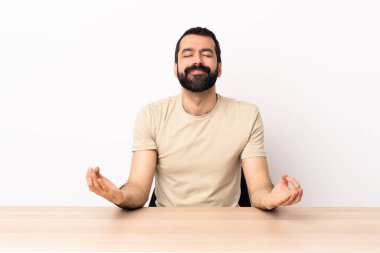 Zen pozunda bir masada sakallı beyaz bir adam..