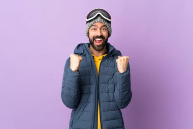 İzole edilmiş mor arka planda snowboard gözlüklü kayakçı galibiyeti kutluyor.