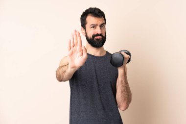 Sakallı, beyaz tenli bir sporcu izole edilmiş arka planda ağırlık kaldırıyor.