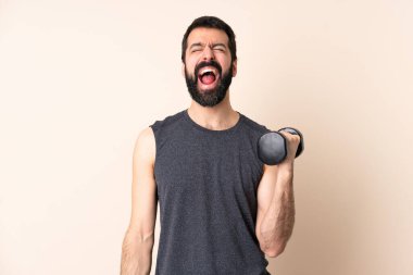 Beyaz sakallı sporcu arka planda halter kaldırıyor ve ağzı açık bağırıyor.