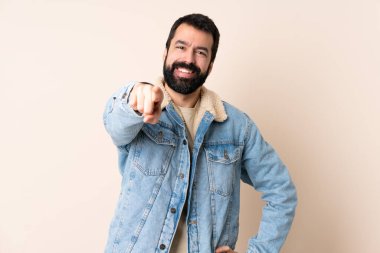 İzole edilmiş arka planda sakallı beyaz adam mutlu bir ifadeyle ön tarafı işaret ediyor.